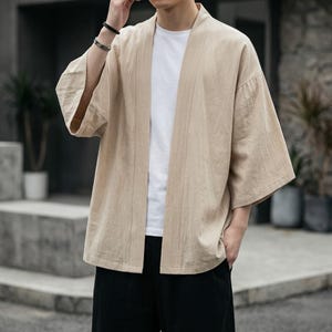 May include: A beige kimono-style jacket with wide sleeves. The open-front jacket is made of a lightweight fabric and is worn over a white t-shirt and black pants. The jacket has vertical lines and a relaxed fit, suitable for casual wear.
