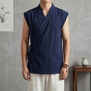Puede incluir: Una camiseta sin mangas azul marino con cuello en V cruzado. La parte superior está hecha de una tela texturizada y tiene un cierre de lazo en el lateral. El modelo lleva pantalones blancos y una pulsera de cuentas de madera. Estilo japonés.