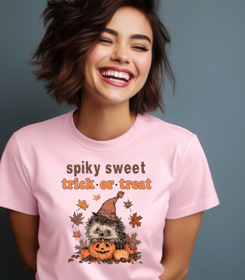May include: Pink t-shirt with a graphic of a hedgehog wearing a witch hat and holding a pumpkin. The text "spiky sweet trick or treat" is printed on the shirt.