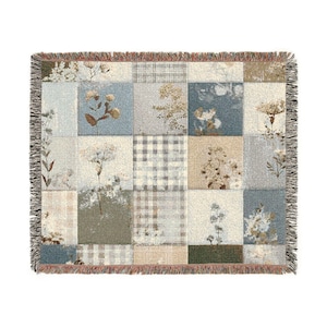 May include: A woven throw blanket with a patchwork design. The squares feature floral patterns and plaid in shades of blue, beige, and grey. The blanket has a fringed edge.