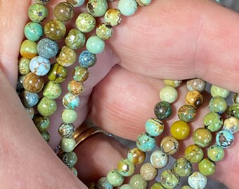 May include: Close-up of several strands of beaded bracelets. The beads are small and round, in shades of green, brown, and turquoise. The bracelets are held in a hand, showcasing the color variations and textures of the beads.