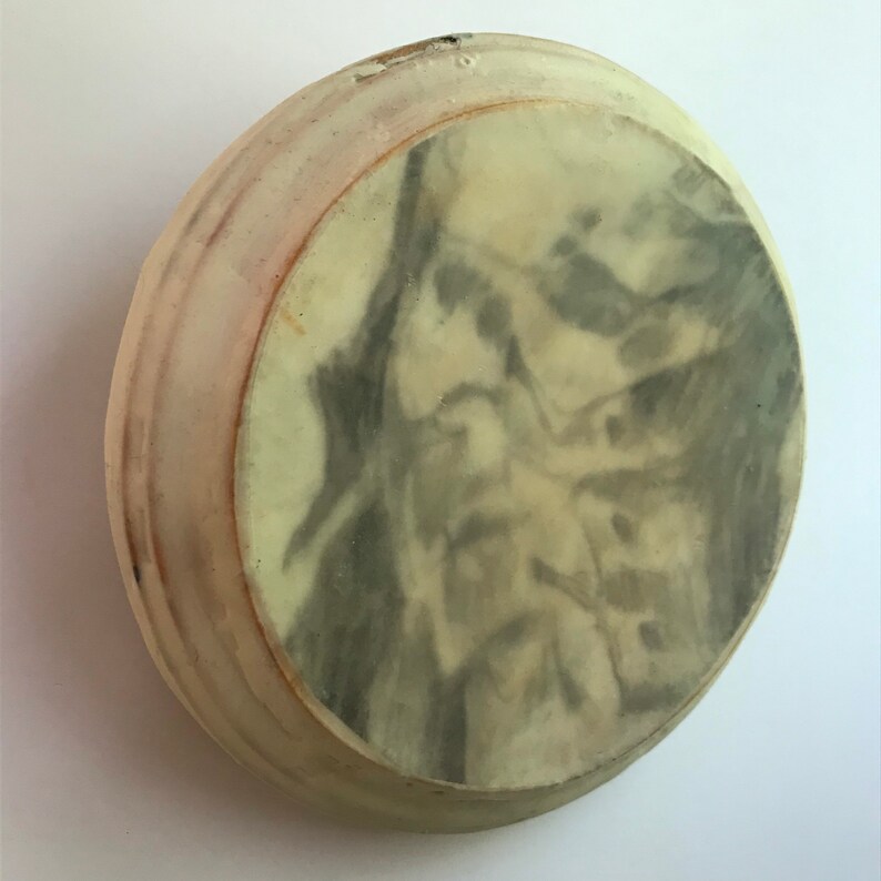 Puede incluir: Un objeto cer&aacute;mico redondo, blanquecino, con un dise&ntilde;o veteado gris y crema en la superficie. El borde tiene un tono marr&oacute;n rojizo ligeramente m&aacute;s oscuro. Parece ser un plato o cuenco peque&ntilde;o.