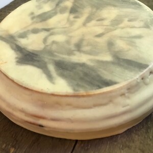 Puede incluir: Un objeto decorativo redondo, blanquecino, con un patr&oacute;n veteado gris y blanco en la superficie superior. El objeto tiene un dise&ntilde;o acanalado y en capas alrededor de los lados. Est&aacute; sobre una superficie de madera.