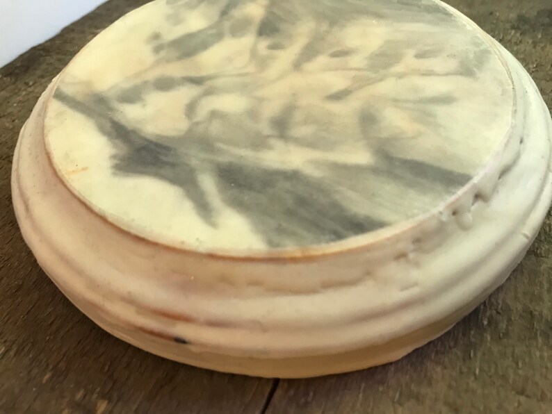 Puede incluir: Un objeto decorativo redondo, blanquecino, con un patr&oacute;n veteado gris y blanco en la superficie superior. El objeto tiene un dise&ntilde;o acanalado y en capas alrededor de los lados. Est&aacute; sobre una superficie de madera.