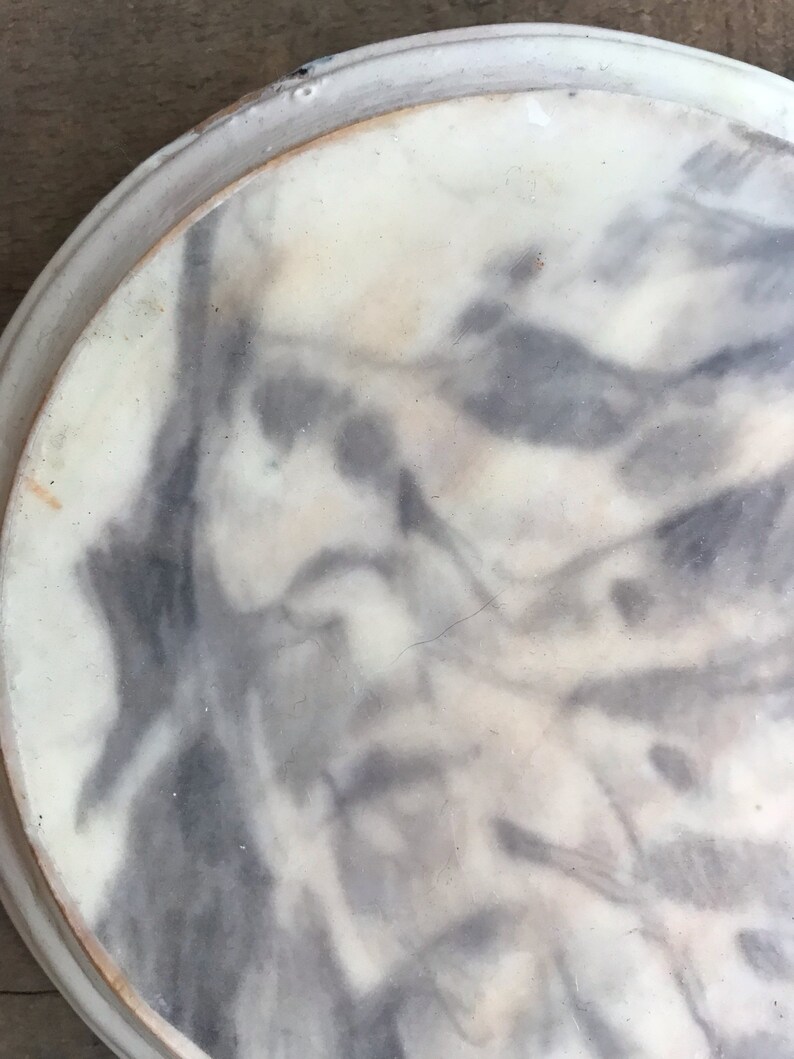 Puede incluir: Un plato redondo, blanquecino, con un patr&oacute;n veteado gris y blanco. El plato tiene un borde elevado y una textura ligeramente rugosa. El dise&ntilde;o se asemeja a una pintura de acuarela.