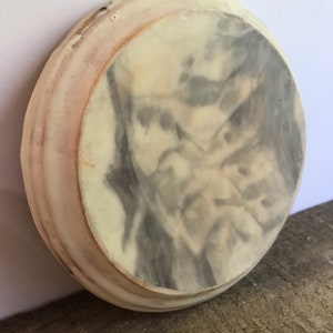 Puede incluir: Un posavasos redondo, blanquecino, con un dise&ntilde;o veteado gris y blanco en el centro. El posavasos tiene un borde ligeramente elevado con un tono rosado. El posavasos est&aacute; hecho de un material s&oacute;lido y parece hecho a mano.