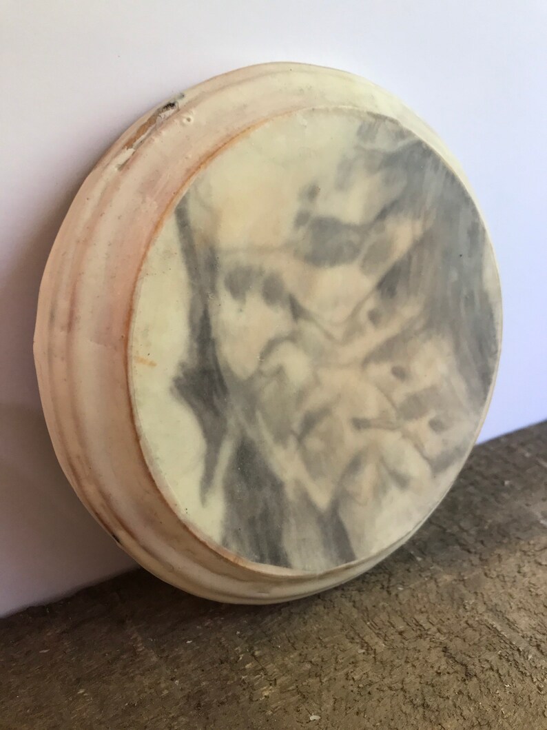 Puede incluir: Un posavasos redondo, blanquecino, con un dise&ntilde;o veteado gris y blanco en el centro. El posavasos tiene un borde ligeramente elevado con un tono rosado. El posavasos est&aacute; hecho de un material s&oacute;lido y parece hecho a mano.