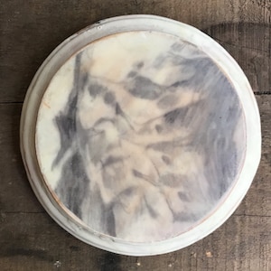Puede incluir: Un plato decorativo redondo con un dise&ntilde;o veteado en tonos grises y crema. Tiene un borde blanco en relieve y una superficie ligeramente texturizada. Ideal para servir o exhibir, con un di&aacute;metro de unos 25 cm.