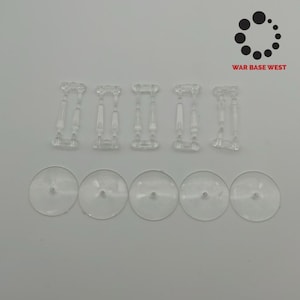 Puede incluir: Un conjunto de soportes y bases de plástico transparente para modelos en miniatura. Los soportes son rectangulares con un soporte central, y las bases son circulares con un agujero central. El texto "WAR BASE WEST" está en la esquina superior derecha.