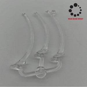 May include: Clear plastic model kit parts for a ship's masts. The parts are curved and have small circular details. WAR BASE WEST is printed on the background.