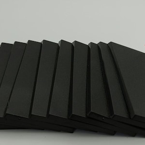 May include: A stack of ten black rectangular foam tiles. The tiles are arranged in a fan shape. The tiles are for use in wargaming.