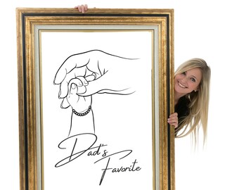 May include: A black and white line drawing of a hand holding a smaller hand, with the text "Dad's Favorite" below. The drawing is framed in a gold frame and a woman is peeking out from behind the frame.