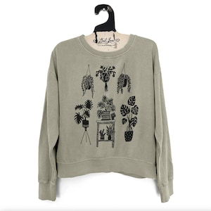 Sudadera semicorta de mujer, color verde salvia, teñida en prenda, con estampado de plantas de interior en la ventana.