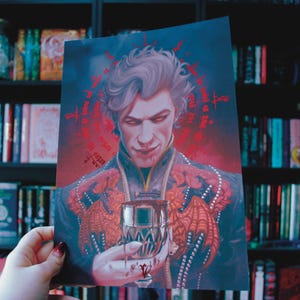 Puede incluir: Una impresión que presenta un retrato de un hombre con piel pálida, ojos rojos y cabello gris, sosteniendo un vaso. La obra de arte tiene una estética oscura y gótica con acentos y texto rojos. El fondo es una estantería.