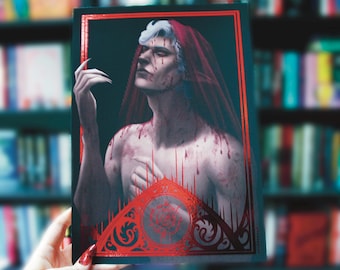 Puede incluir: Una portada de libro con una figura pálida y ensangrentada que lleva una capucha roja. La figura tiene una mano en forma de garra levantada y está rodeada de un marco rojo adornado.