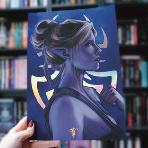 May include: A print featuring a side profile of a woman with pointed ears and a bun, rendered in shades of purple and blue. The background is a dark blue with holographic accents. A small gold emblem is visible at the bottom.