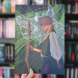 Puede incluir: Lámina artística que presenta un personaje con orejas puntiagudas, sosteniendo un báculo, sobre un fondo verde y dorado con un contorno de lobo. El personaje viste un atuendo verde y blanco con detalles dorados. La obra tiene una temática fantástica.