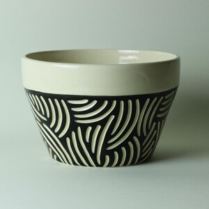 May include: A white ceramic bowl with a black and white geometric pattern. The bowl is slightly flared at the top and has a rounded bottom.