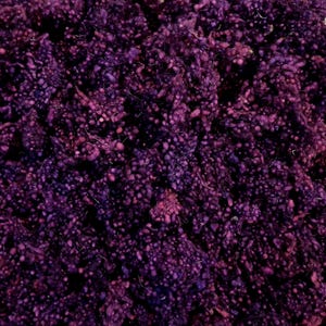 May include: Close-up of a pile of textured, deep purple yarn. The yarn has a nubby, irregular texture with small, raised bumps throughout. The color varies slightly, with hints of pink and lighter purple interspersed.