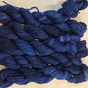May include: Several skeins of hand-dyed yarn in varying shades of blue. The yarn appears to be a soft, natural fiber, with subtle variations in color throughout each skein. The yarn is arranged in a neat, organized manner, suggesting it is ready for use in a knitting or crochet project.