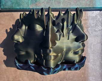 May include: A 3D printed sculpture of three faces, each with a unique expression, is made of a dark green and blue iridescent material. The faces are intertwined and appear to be emerging from a wave-like base.