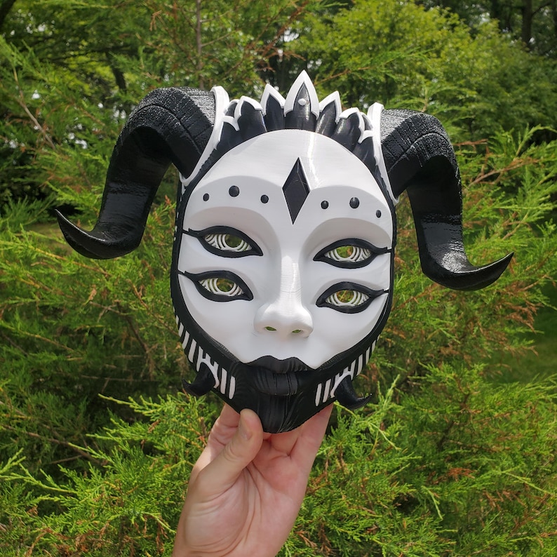 May include: A white and black mask with horns and four eyes. The mask has a detailed design with black and white patterns.