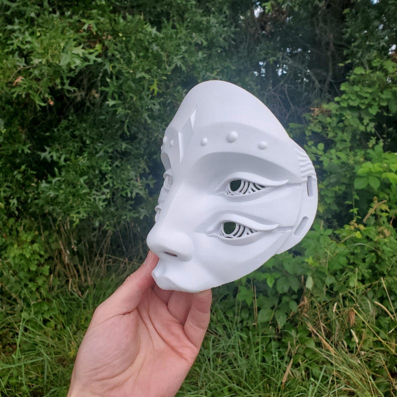 May include: White mask with three eyes, two of which are detailed with intricate cutouts. The mask has a raised, textured design around the eyes and forehead.