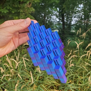 May include: A blue and purple geometric sculpture made of stacked rectangular blocks. The sculpture is made of a shiny material and has a modern design.