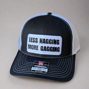 May include: Black and white trucker hat with the text "LESS NAGGING MORE GAGGING" on a white patch. The hat has a black brim and crown, a white mesh back, and a Richardson tag.