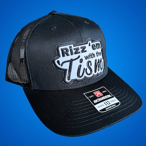 May include: Black trucker hat with a black mesh back. The front of the hat has a white and black embroidered patch that says "Rizz'em with the Tism". The hat has a black adjustable strap with a red and white Richardson logo.