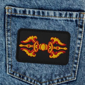 Puede incluir: Vaqueros azul claro con un parche negro en el bolsillo trasero. El parche presenta un diseño simétrico en rojo, amarillo y dorado sobre un fondo negro. Los vaqueros tienen un diseño clásico de cinco bolsillos.