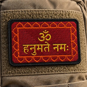 May include: A rectangular embroidered patch attached to a tan tactical backpack. The patch features a deep red background with a yellow Om symbol and the Sanskrit text "हनुमते नमः" in yellow, surrounded by a decorative orange border and black trim.