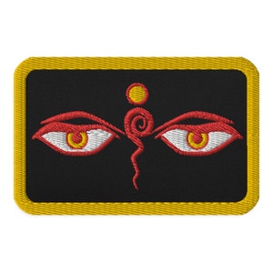 May include: A black embroidered patch with a yellow border. The patch features a stylised image of two red eyes with white pupils and yellow irises. A red and yellow swirl design is centred between the eyes.