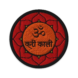 Puede incluir: Un parche redondo bordado con un diseño de mandala rojo y naranja. El centro del mandala presenta el símbolo Om y el texto "करी काली" en negro.