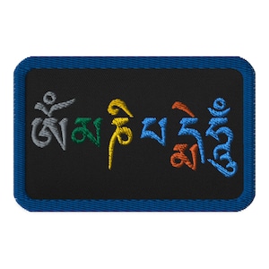 Puede incluir: Un parche bordado azul con la frase tibetana "Om Mani Padme Hum" en letras de colores sobre un fondo negro.