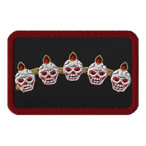 May include: Embroidered patch featuring five stylized skull designs with red accents and flames, connected by a gold-colored line. The patch has a black background with a red border.