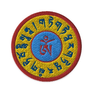 May include: A round, embroidered patch with a red border, a yellow background, and a blue center. The center features a stylized symbol in blue and red. The yellow background is inscribed with a circle of Tibetan script in gold.
