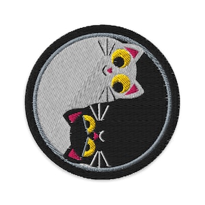 May include: Embroidered patch featuring a yin-yang design with two stylized cats. One cat is white, the other black, with yellow eyes and pink accents. The patch is circular with a black border and a gray background.