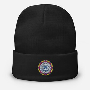 May include: Black beanie with a colorful embroidered mandala design. The mandala features a white center with a blue eye, surrounded by pink and yellow petals.