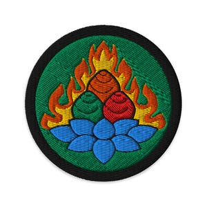 Puede incluir: Parche bordado con un diseño central de una flor de loto azul, tres vainas estilizadas en rojo, verde y naranja, coronadas por llamas. El parche tiene un fondo verde y un borde negro.