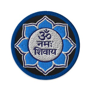 May include: A circular embroidered patch featuring a blue lotus flower design with a white center. The center displays the Sanskrit text Om Namah Shivaya in dark blue embroidery. The patch has a dark blue border and a black background.