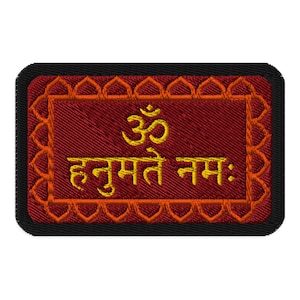 May include: A rectangular embroidered patch featuring a deep red background with a gold-colored Om symbol and the Sanskrit text "हनुमते नमः" in gold thread. The patch is framed by an orange scalloped border and a solid black outer edge.