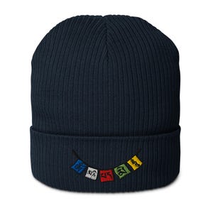 Pode incluir: Um gorro azul marinho com textura canelada. O gorro apresenta um pequeno desenho bordado de bandeiras de oração coloridas. As bandeiras são em tons de azul, vermelho, verde e amarelo.