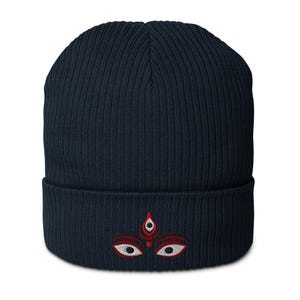 May include: A navy blue knitted beanie with a red and white embroidered design of a stylized eye with a third eye in the center.