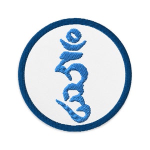 Op de afbeelding: Een blauw geborduurd Om-symbool op een witte ronde patch met een donkerblauwe rand.