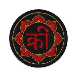 May include: Embroidered patch with a black background, featuring a red symbol in the center and a ring of red petal-like shapes around it. The symbol is written in red. The patch is round with a gold border.