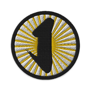 May include: An embroidered patch featuring a large black number one in the centre. The number one is surrounded by a circle of white and gold rays.