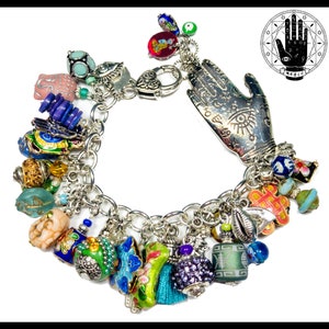 May include: Silver charm bracelet with a variety of colorful charms. Charms include a hand with an eye, beads, and other decorative elements. The bracelet has a lobster clasp and a chain link design. The word "magic" is in the image.