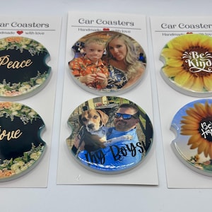 May include: Car coasters with various designs. Some feature floral arrangements with the words "Peace" and "Love." Others display photos of people and pets. Two coasters have sunflower designs with the phrases "Be Kind" and "Be Happy."