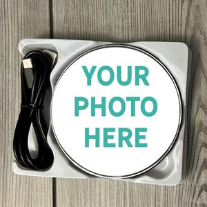 May include: A white wireless charging pad with a silver trim. The pad has the text "YOUR PHOTO HERE" printed on it in teal.